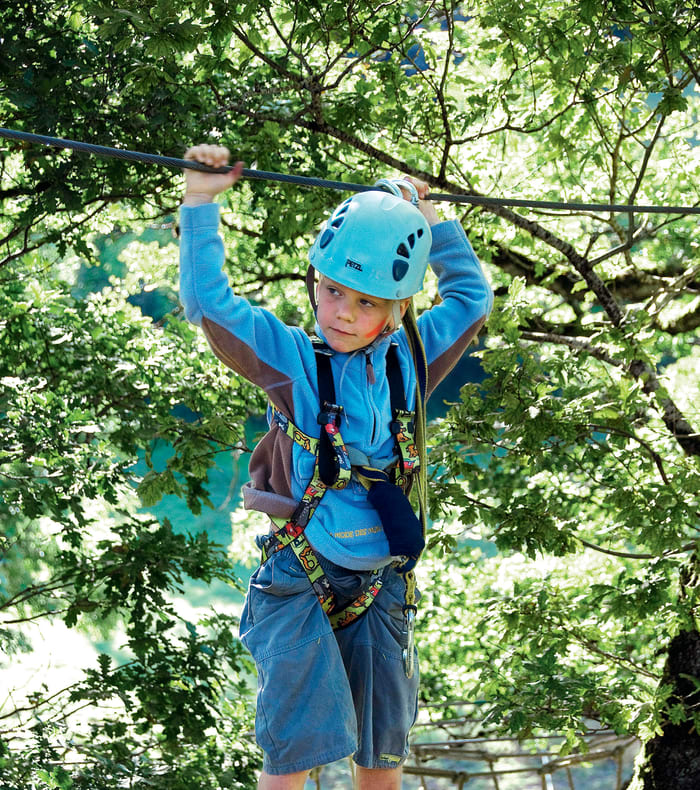 Enfant en parcours acrobatique en forêt avec casque bleu et équipement de sécurité, activité multisports du pony camp