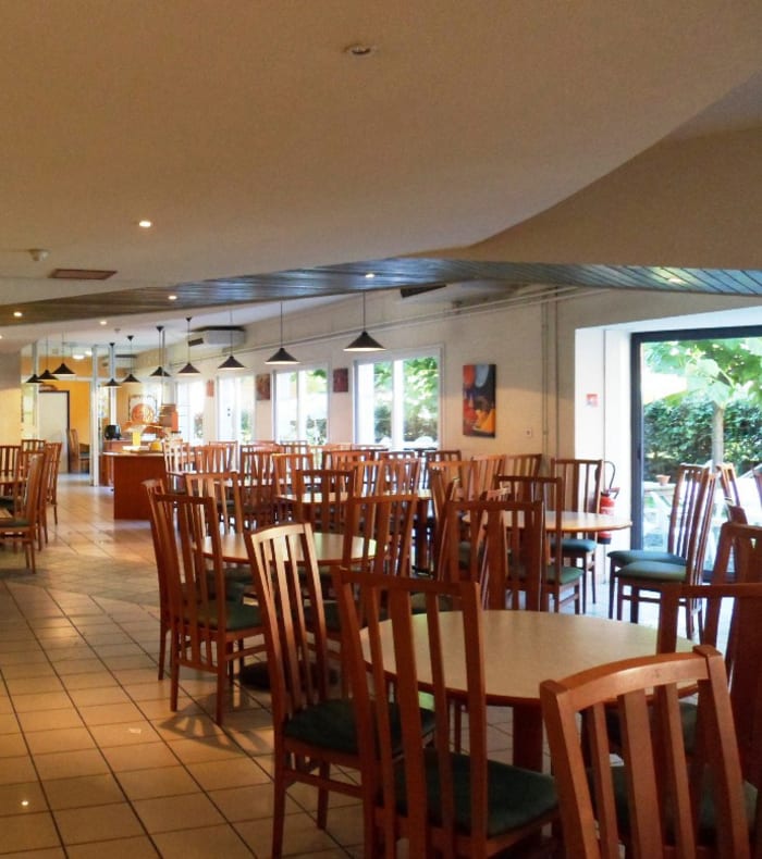 Intérieur spacieux d'un restaurant à Saint-Lary Soulan avec tables en bois, chaises et mobilier moderne, accès terrasse avec vue sur la nature