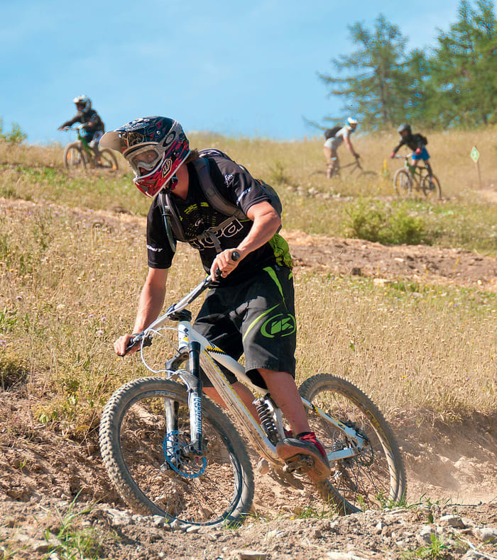 Jeune cycliste en VTT freeride sur terrain accidenté avec groupe d'enfants pratiquant le VTT en arrière-plan dans un cadre naturel ensoleillé