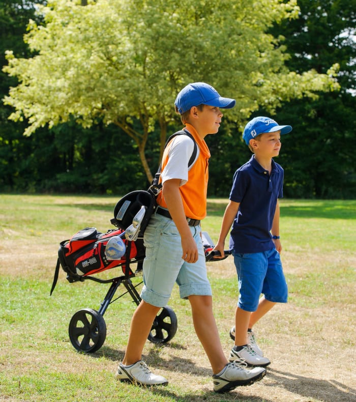Deux jeunes golfeurs en casquette bleue marchant sur un parcours de golf avec un sac de clubs rouges et noir