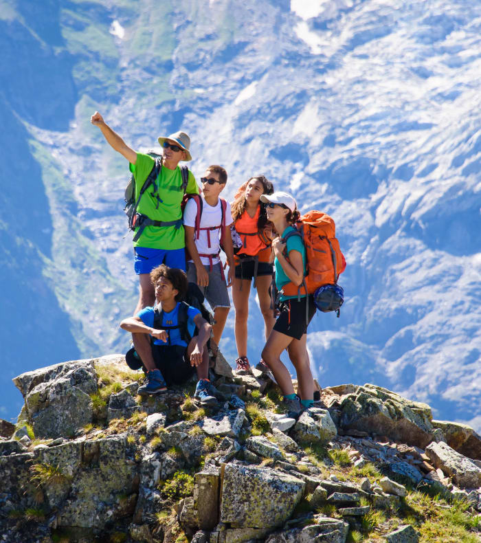Groupe d'adolescents en tenue de randonnée au sommet rocheux surplombant une vallée alpine enneigée