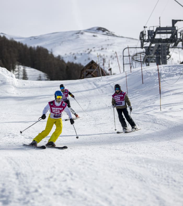 Groupe de skieurs en formation technique sur piste enneigée avec remontée mécanique et montagne en arrière-plan