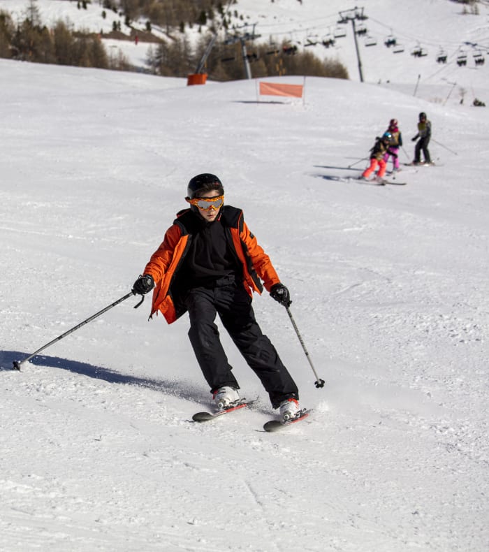 Jeune skieur en veste orange dévale les pentes enneigées des Orres avec d'autres skieurs et snowboarders en arrière-plan