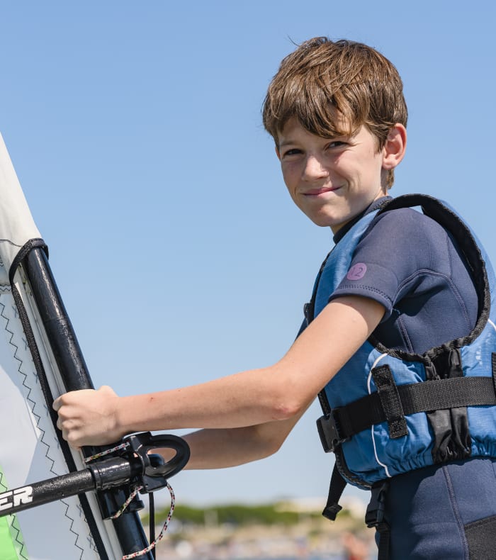Jeune pratiquant de windsurf tenant une voile verte fluo avec gilet de sauvetage bleu par beau temps