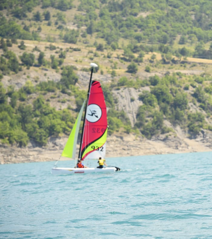 Pratiquant de kite et de voile à Embrun sur un lac turquoise avec montagnes boisées en arrière-plan