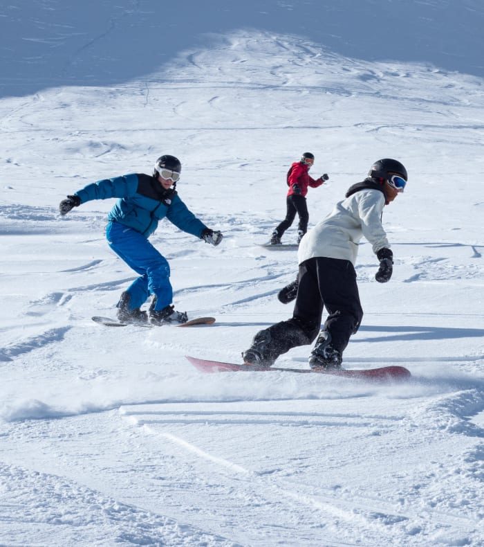 Groupe de jeunes snowboarders en freestyle sur piste enneigée aux Arcs avec moniteur en veste bleue