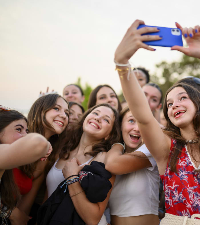 Groupe d'adolescents en Corse prenant un selfie collectif avec un smartphone bleu, sourires joyeux et paysage naturel en arrière-plan