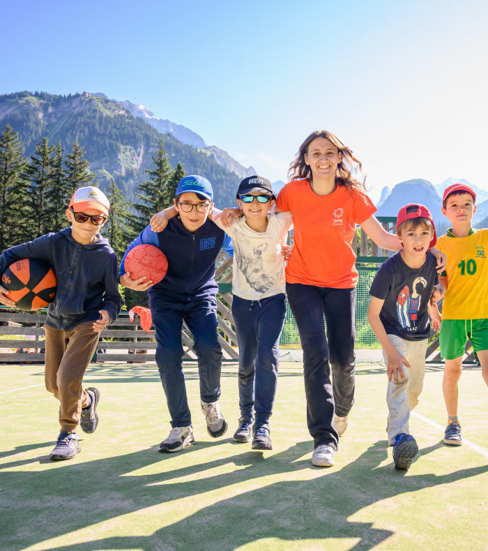 Groupe d'enfants pratiquant le multisports en montagne avec ballons et équipements sportifs sur terrain en vallée alpine