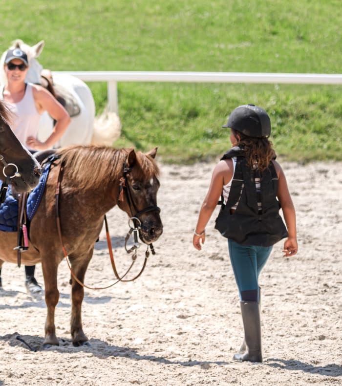 Enfants en équitation à Valloire avec moniteur et chevaux sellés dans un enclos herbeux