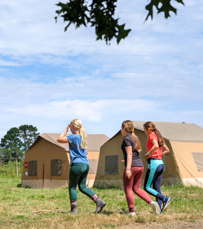 Jeunes cavaliers en tenue équestre courant près des tentes du séjour équitation en Bretagne