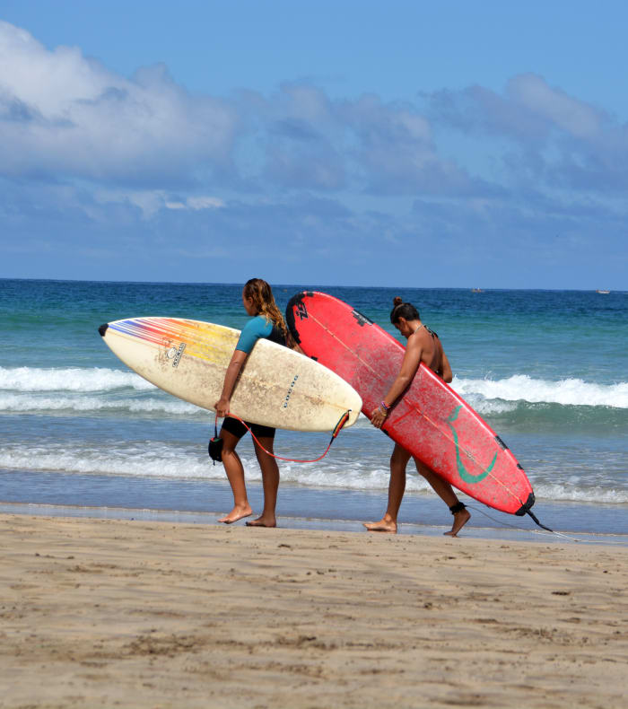Jeunes surfeurs portant leurs planches sur une plage de Martinique avec vagues turquoise et ciel dégagé