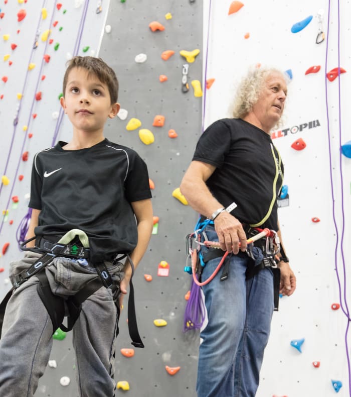 Jeune enfant et moniteur d'escalade préparant une séance sur mur d'escalade intérieur avec prises colorées