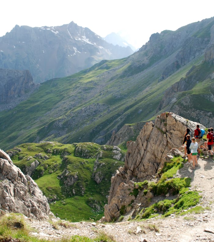 Groupe de randonneurs en montagne à Serre Chevalier avec pics rocheux et vallée verdoyante pour séjour Five Summits