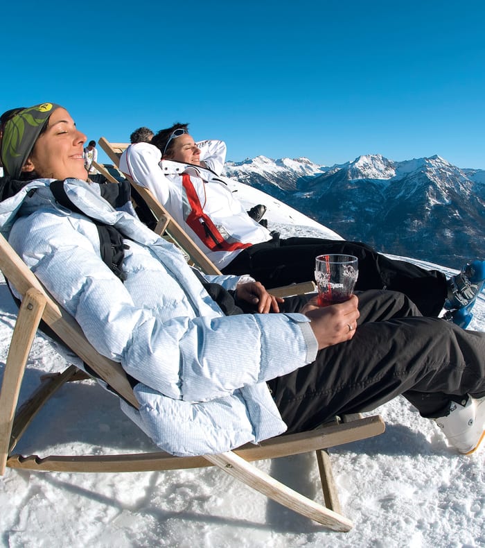 Deux personnes relaxant en chaises longues sur une terrasse enneigée avec vue panoramique sur les montagnes de Serre Chevalier
