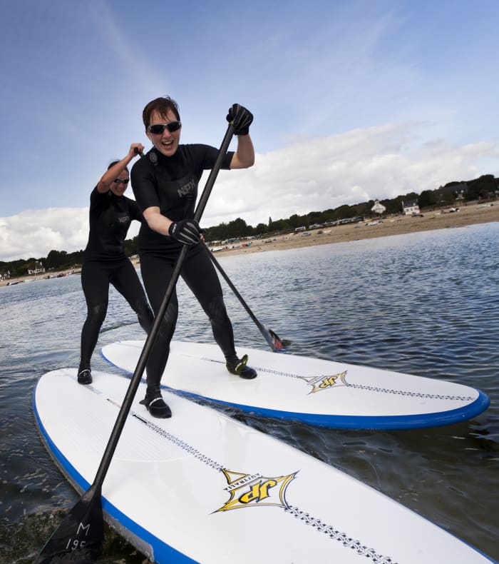 Moniteur en combinaison noire pratiquant le stand up paddle en mer lors d'une initiation nautique