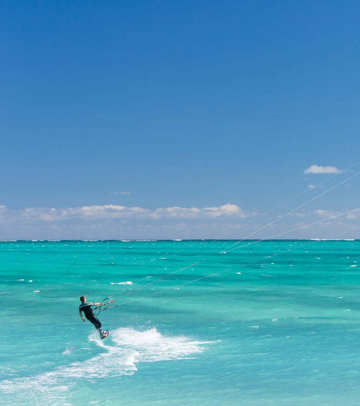 Kitesurfeur en action sur une mer turquoise avec cerf-volant rouge et noir, spot de croisière kitesurf débutant