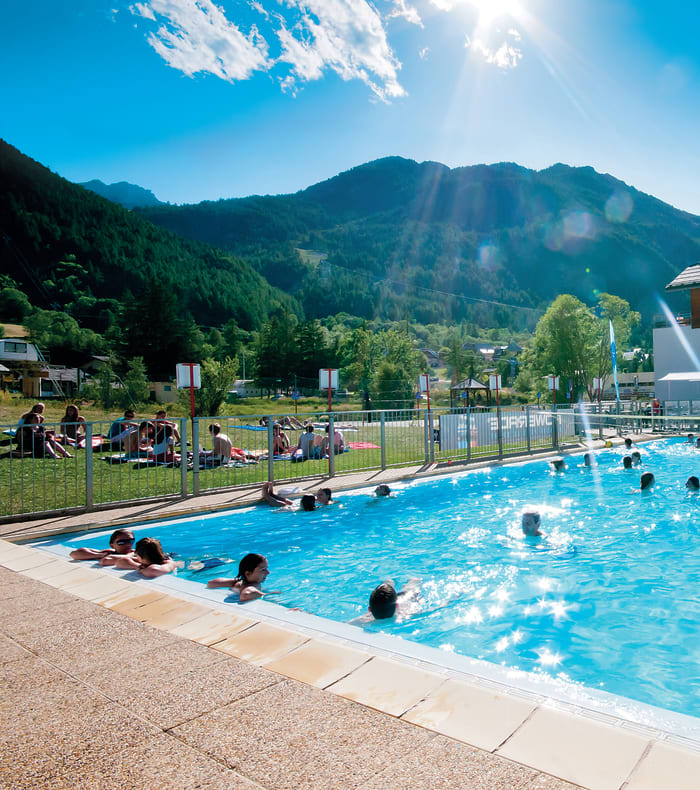 Centre de séjour en montagne avec piscine, jeunes en activités aquatiques et montagnes du Briançonnais en arrière-plan