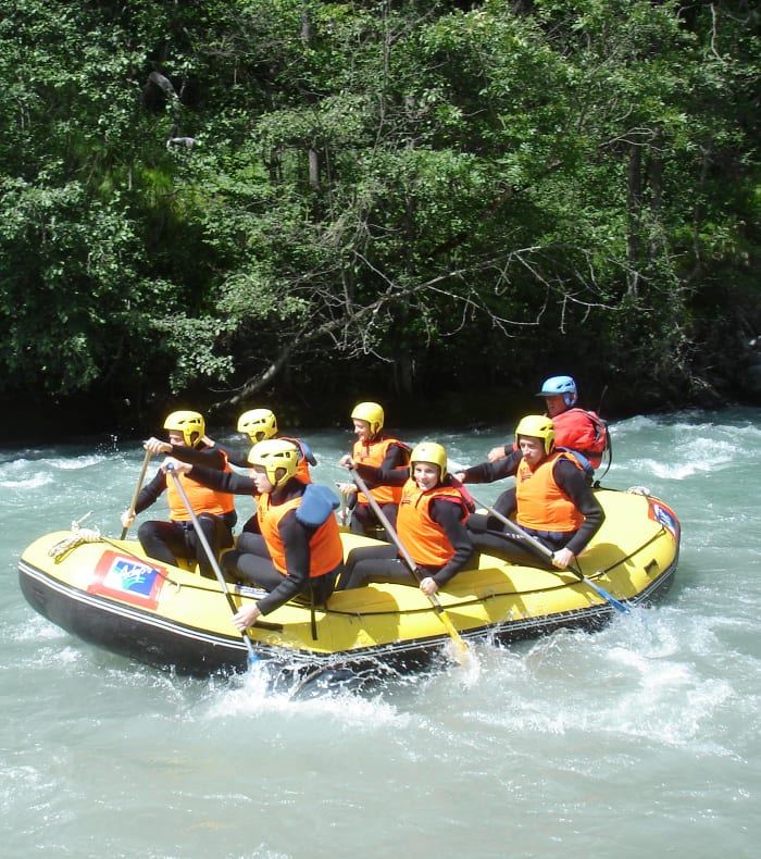 Groupe de jeunes en rafting équipés de gilets de sauvetage orange navigant sur eaux vives turquoise entourées de forêt dense