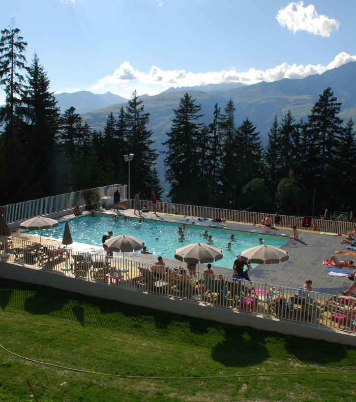 Piscine extérieure avec vue panoramique sur les montagnes enneigées aux Arcs, entourée de sapins et parasols