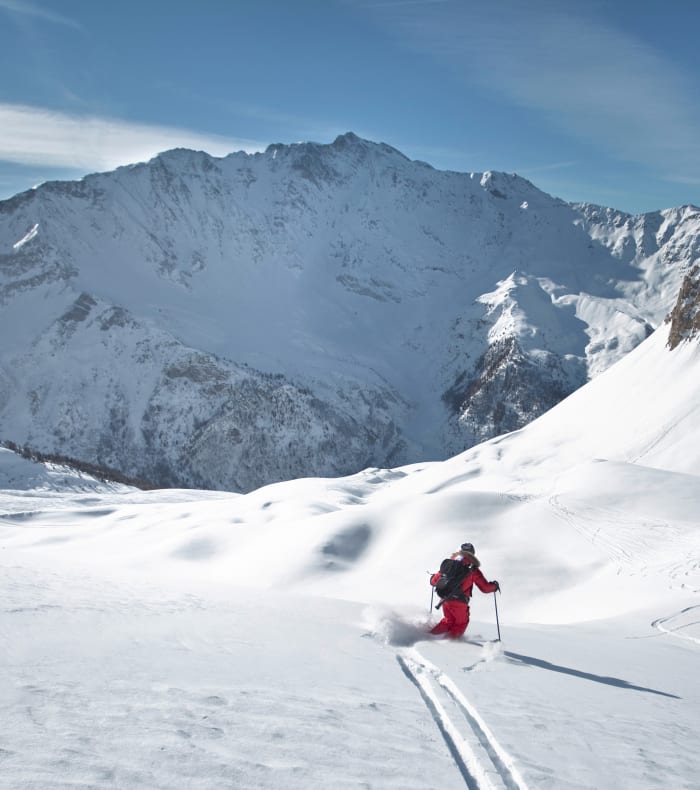 Skieur en pente forte hors-piste dans les Alpes avec sommets enneigés en arrière-plan
