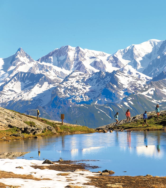Groupe de jeunes randonneurs au lac alpin avec sommets enneigés de la Vanoise en arrière-plan