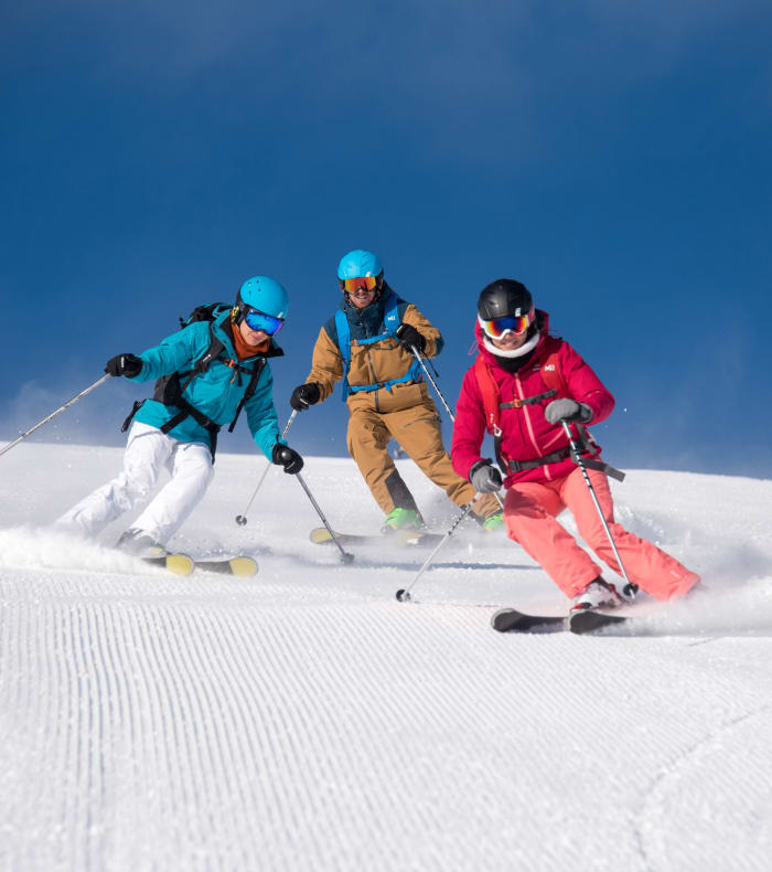 Trois skieurs descendant une piste enneigée à Serre-Chevalier sous un ciel bleu dégagé