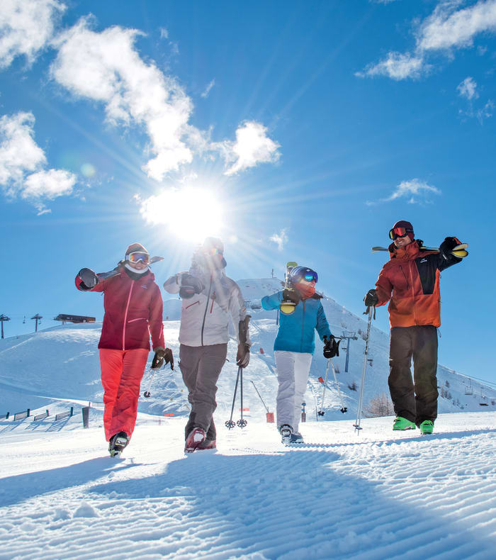 Groupe de skieurs marchant sur les pistes enneigées de Serre Chevalier sous un ciel bleu ensoleillé