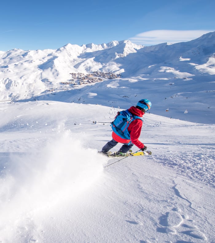 Skieur en descente hors-piste sur un versant enneigé avec vue panoramique sur les montagnes alpines et la vallée