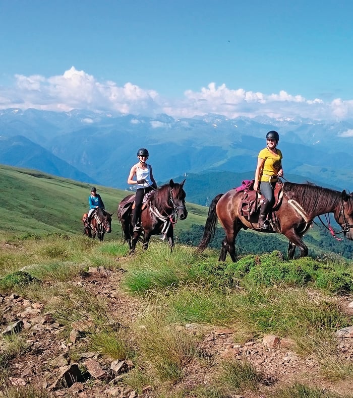Cavaliers en randonnée équestre sur les plateaux verdoyants des Pyrénées avec vue sur les chaînes de montagnes