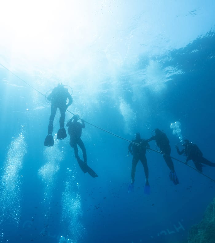 Groupe de plongeurs en équipement de plongée explorant les profondeurs sous-marines avec rayons de lumière naturelle