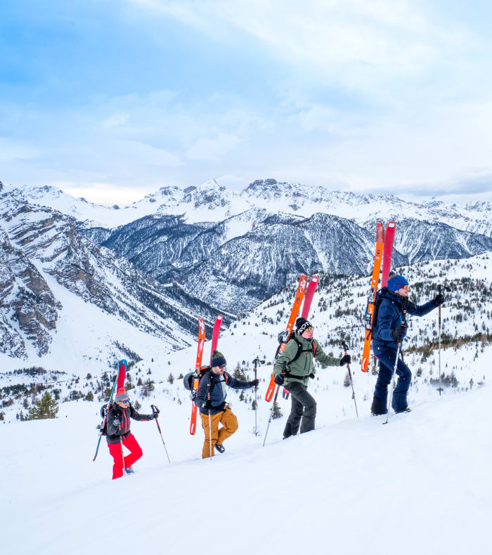 Groupe de randonneurs en ski de rando itinérant en montagne enneigée avec refuges alpins visibles en arrière-plan