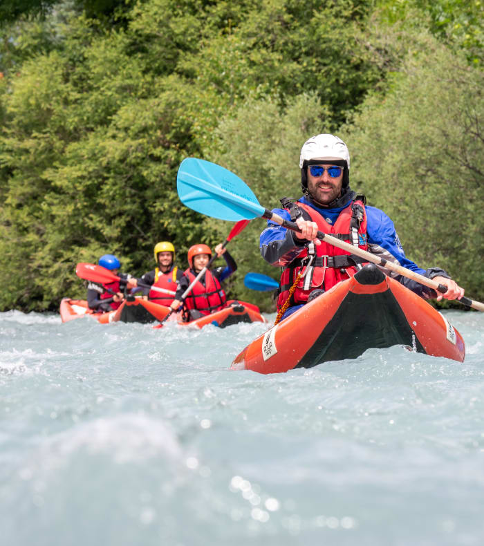 Kayakiste en eaux vives avec pagaie bleue, groupe de rafting en arrière-plan sur rivière de montagne