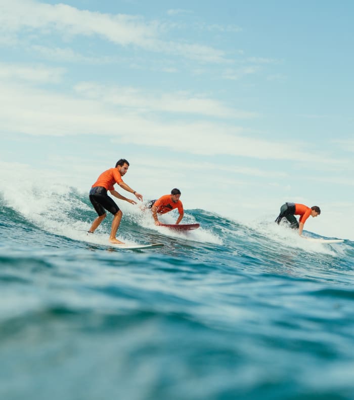 Groupe de surfeurs en session de cours à La Torche, glissant sur des vagues avec moniteur et participants en gilets de sauvetage orange