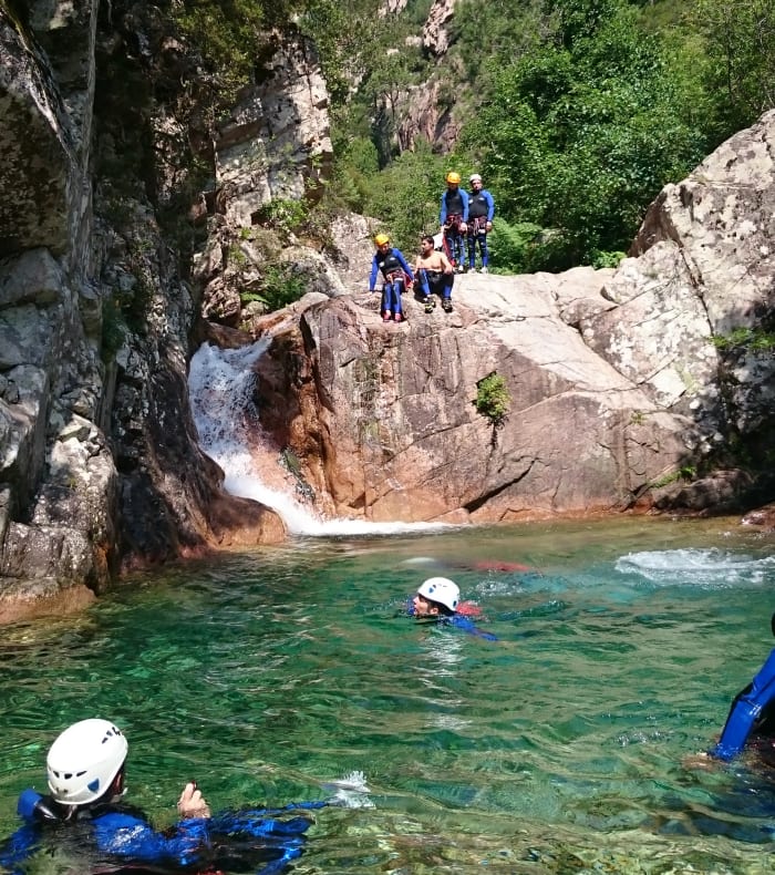 Groupe de canyonieurs en équipement de protection explorant une cascade et des bassins rocheux en Corse