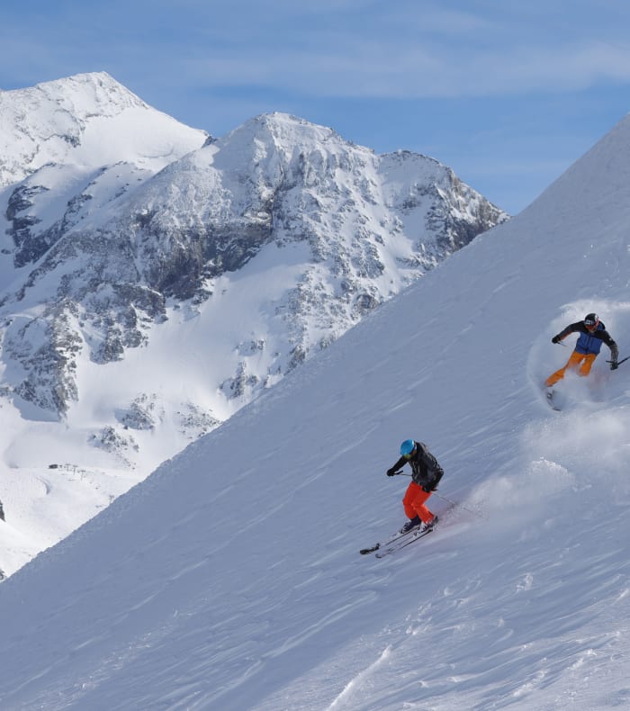 Skieur et snowboardeur descendant une pente enneigée avec massif montagneux enneigé en arrière-plan