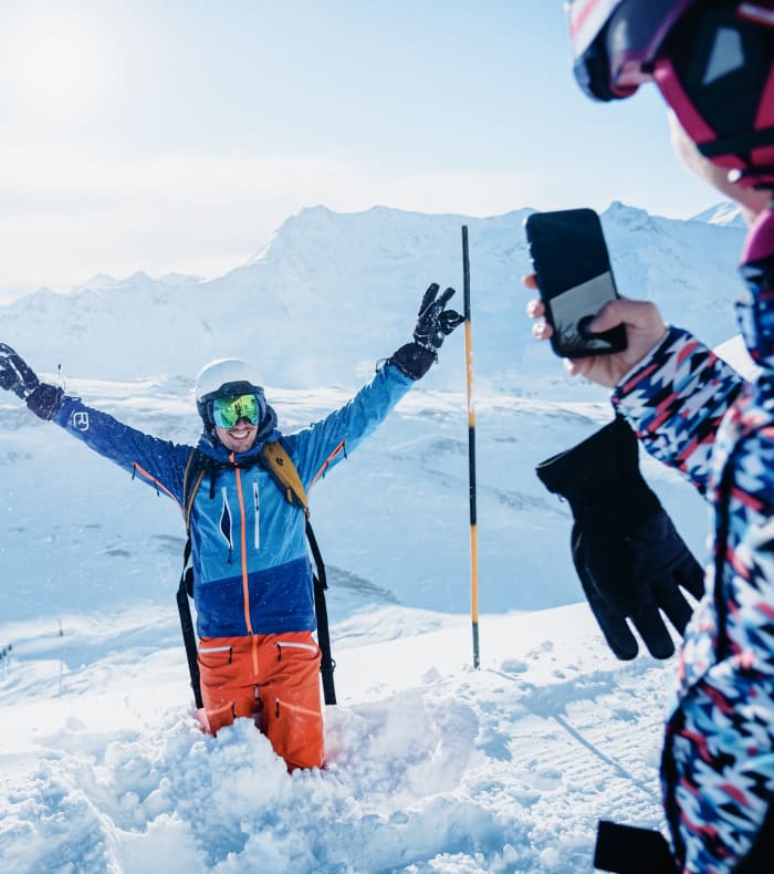 Skieur en hors-piste à Chamonix, bras levés en célébration, entouré d'amis dans la neige avec vue sur les montagnes enneigées
