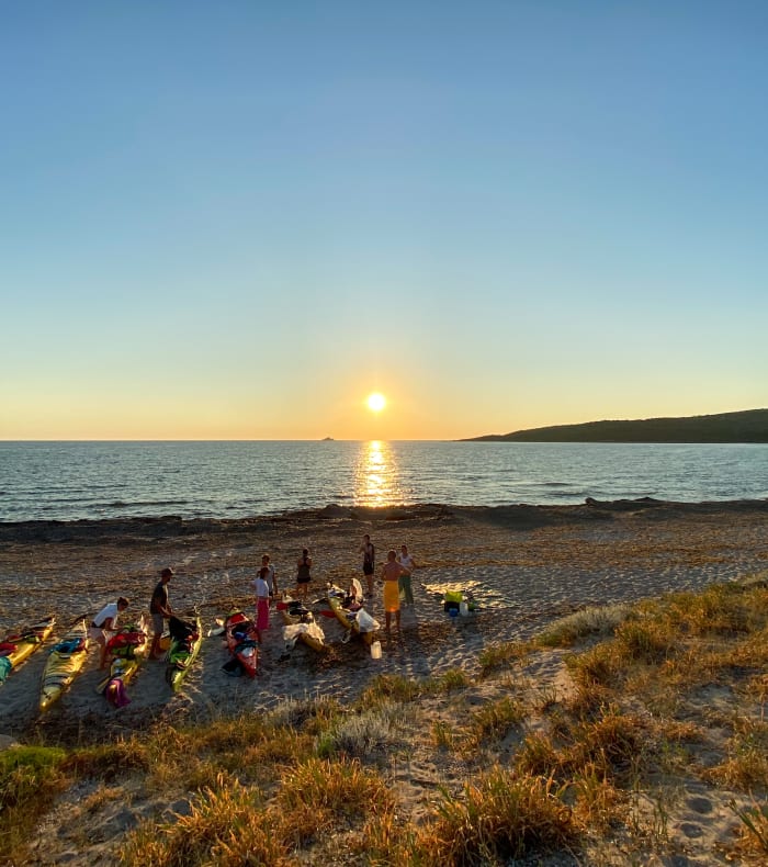 Groupe de jeunes en activité multisports sur une plage de Corse au coucher de soleil avec kayaks alignés