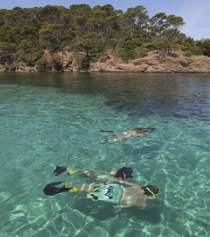 Adolescents en palmes pratiquant le snorkeling en eaux turquoise avec vue sur côte rocheuse boisée de Corse