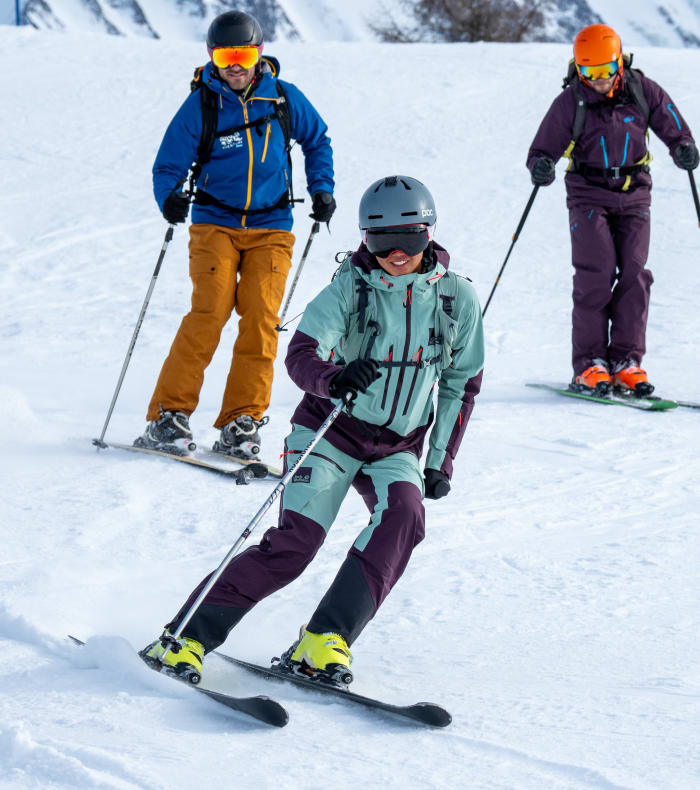 Trois skieurs en équipement coloré descendant une piste enneigée de Saint Lary avec montagnes en arrière-plan