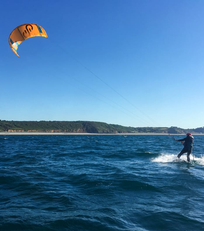 Kitesurfeur en action à Erquy avec voile jaune et orange, falaises bretonnes en arrière-plan