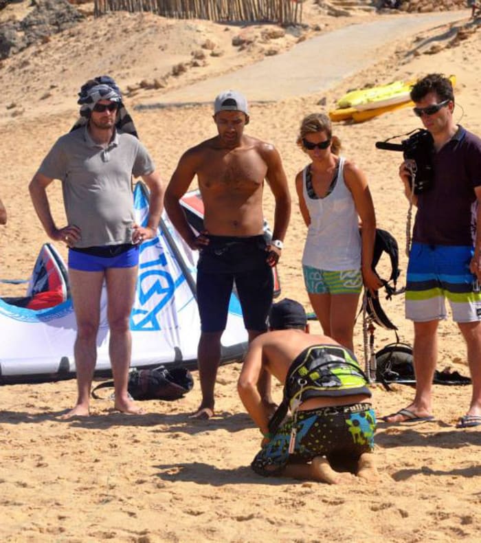 Groupe de débutants en kitesurf sur une plage de sable blanc recevant une formation avec équipement et cerfs-volants