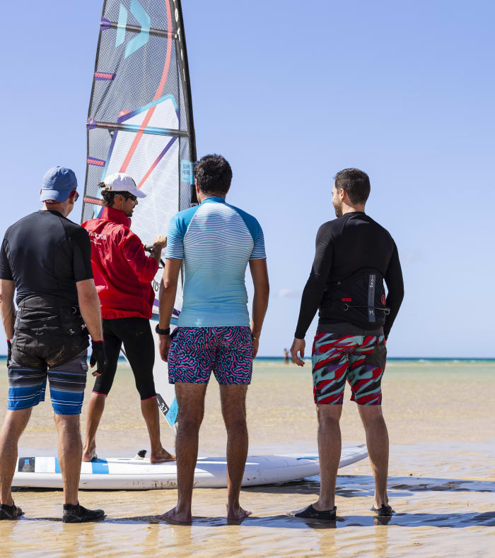 Groupe de windsurfeurs sur la plage préparant leur matériel avec voile colorée et planche avant de prendre la mer