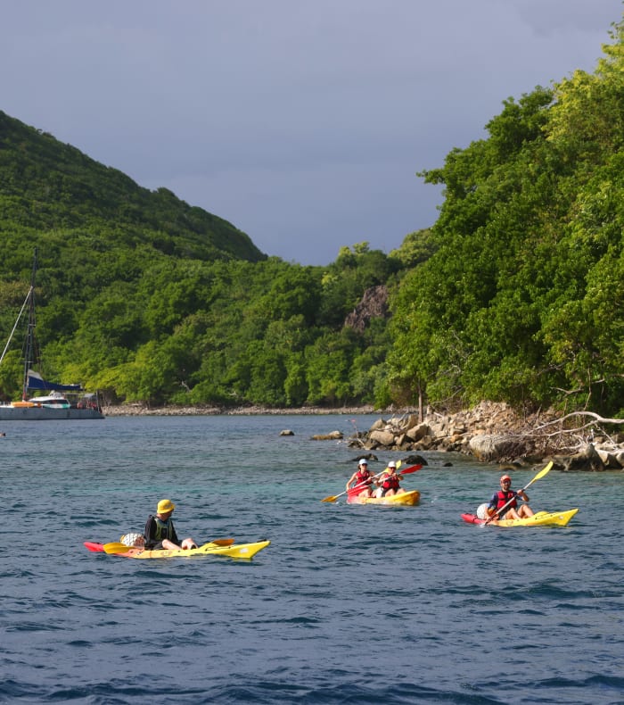 Baie tropicale des Saintes avec voiliers et groupe de kayakistes en eaux turquoise entourés de végétation luxuriante