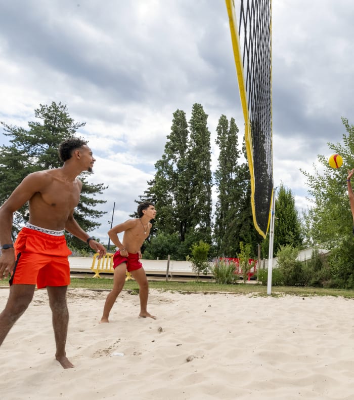 Groupe de joueurs en action sur un terrain de beach-volley avec filet jaune et ballon, lors d'un stage multisports à l'UCPA