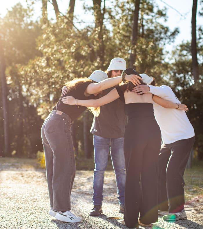 Groupe d'enfants en cercle se donnant un câlin collectif dans une forêt ensoleillée pour une activité de coopération et d'entraide