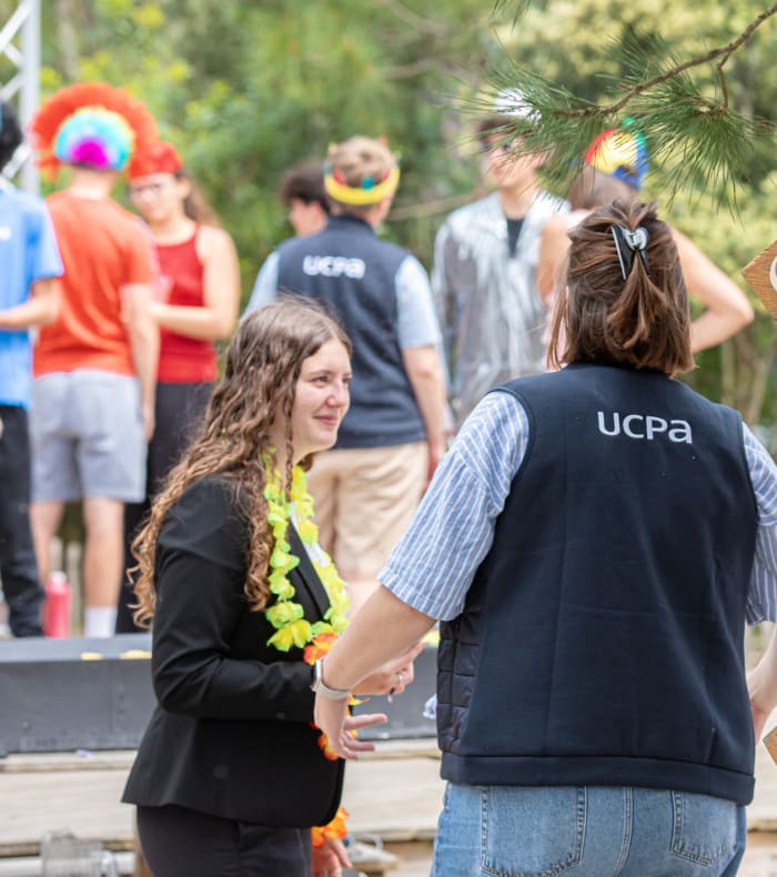 Jeune femme portant un gilet UCPA à Bombannes avec panneaux d'activités de loisirs et formateurs en arrière-plan