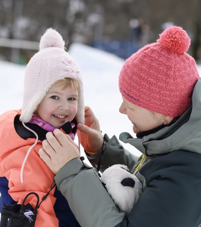Famille jouant dans la neige lors d'un séjour sportif hivernal, enfants et adultes en tenues colorées et chapeaux chauds