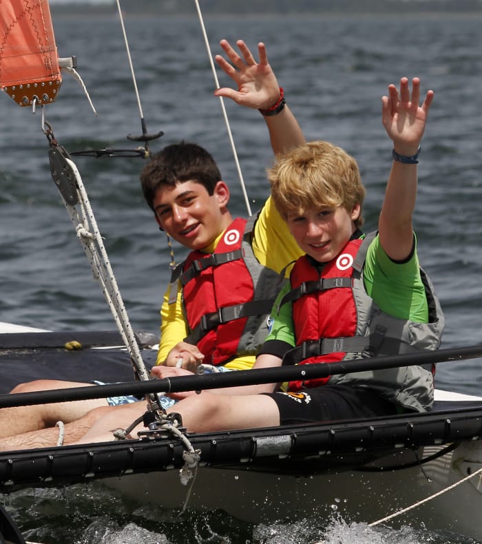 Enfants pratiquant les sports nautiques sur le lac de Bombannes en voilier avec gilet de sauvetage orange, moniteur et paysage lacustre