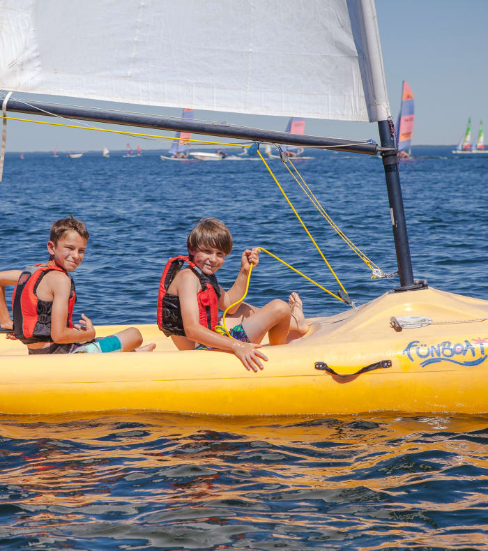 Enfants en classe de mer pratiquant les sports nautiques sur la plage de sable fin de Bombannes avec voiliers et kayaks en mer