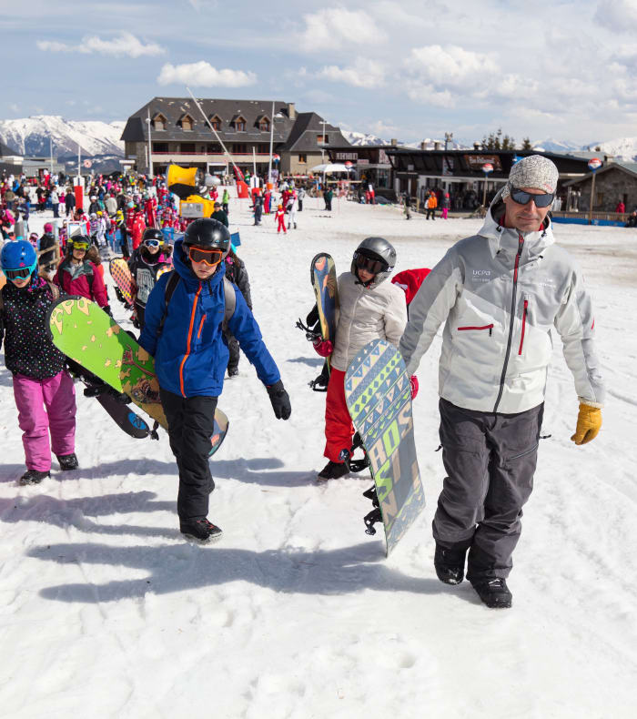 Groupe d'enfants et d'adultes en tenue de ski et snowboard à Saint-Lary Soulan avec montagne enneigée et village sportif en arrière-plan